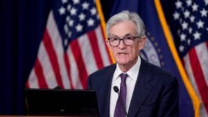 Federal Reserve Chair Jerome Powell speaking from behind a podium with American flags in the background.