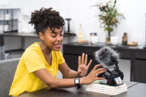 An attractive African American female creates content with a video camera in a bright office.