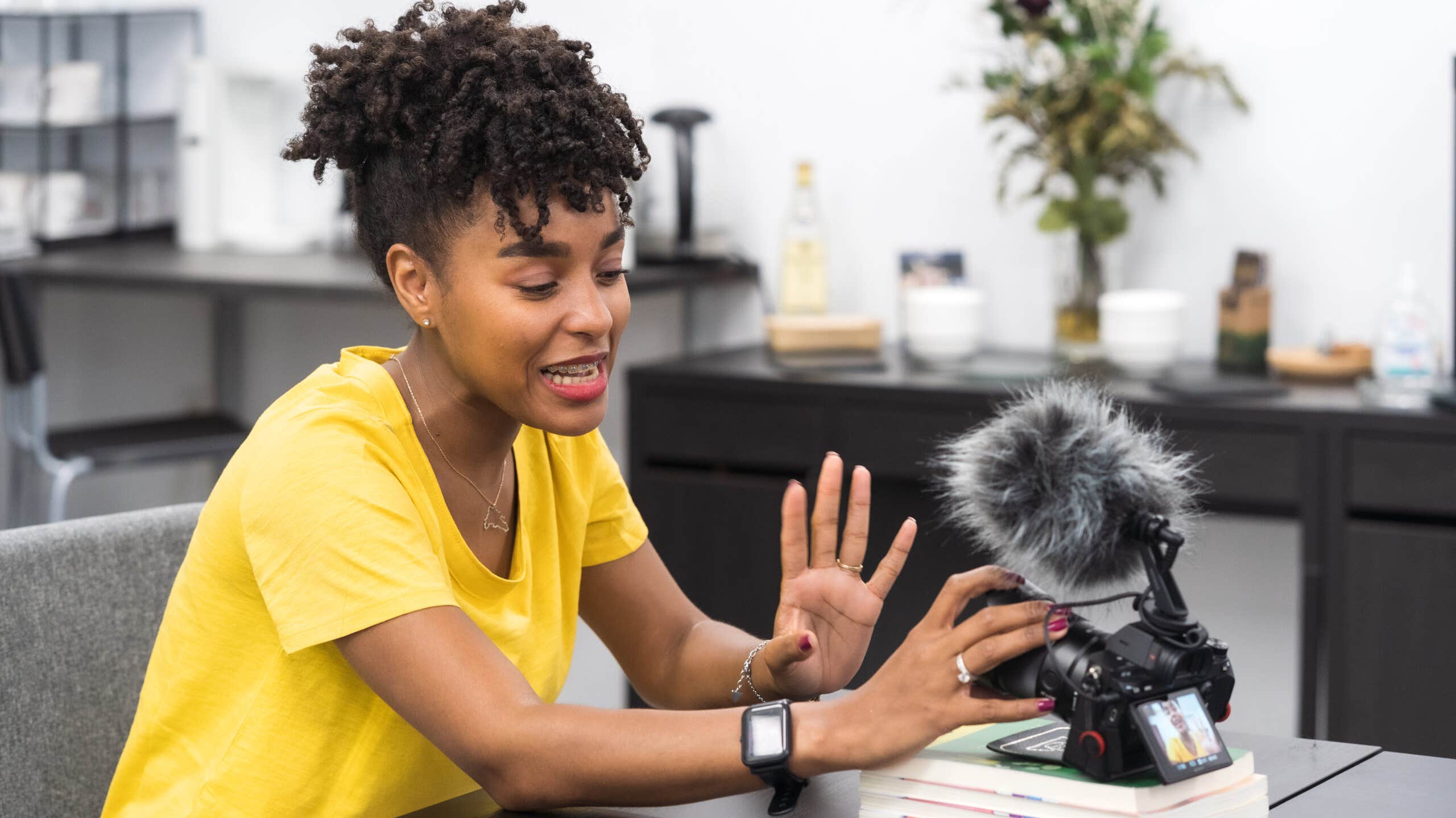 An attractive African American female creates content with a video camera in a bright office.