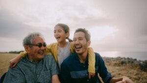 Young girl having fun with her grandfather and father by sea at sunset