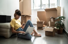 woman online shopping while surrounded by moving boxes in new apartment