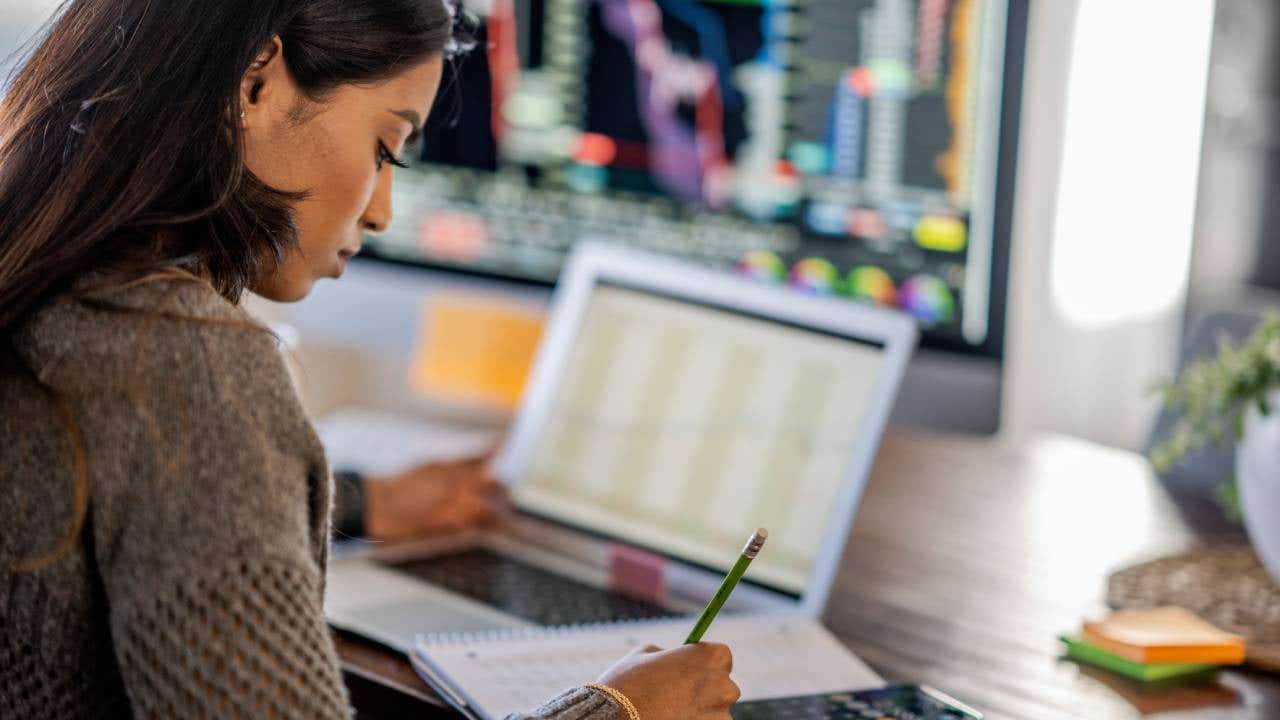 Woman tracking and trading stocks using laptop and desktop computer.