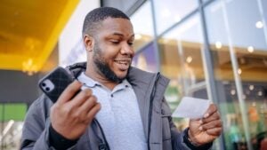 A surprised young man walks outside with a winning lottery ticket in his hands.