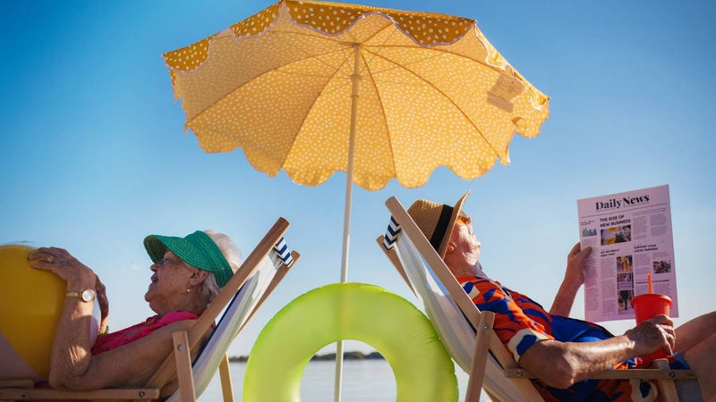 Portrait of a senior couple lying in beach chairs under a sun umbrella.