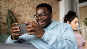 man playing games on his phone sitting next to a woman reading