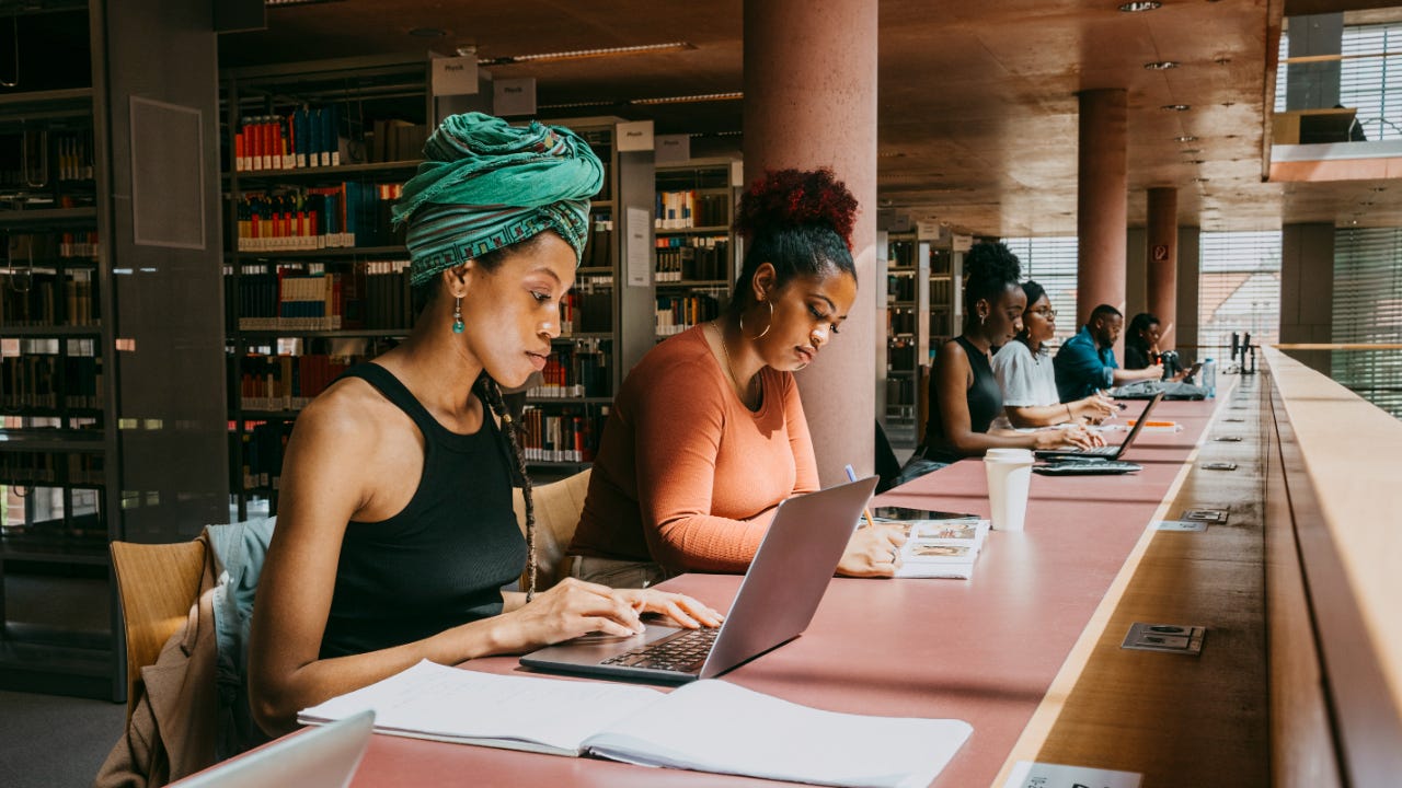 Two women study on laptops in a college library.