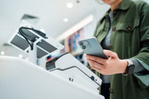 Close up of a person's hand making mobile payment with a smartphone at a self-checkout counter.,