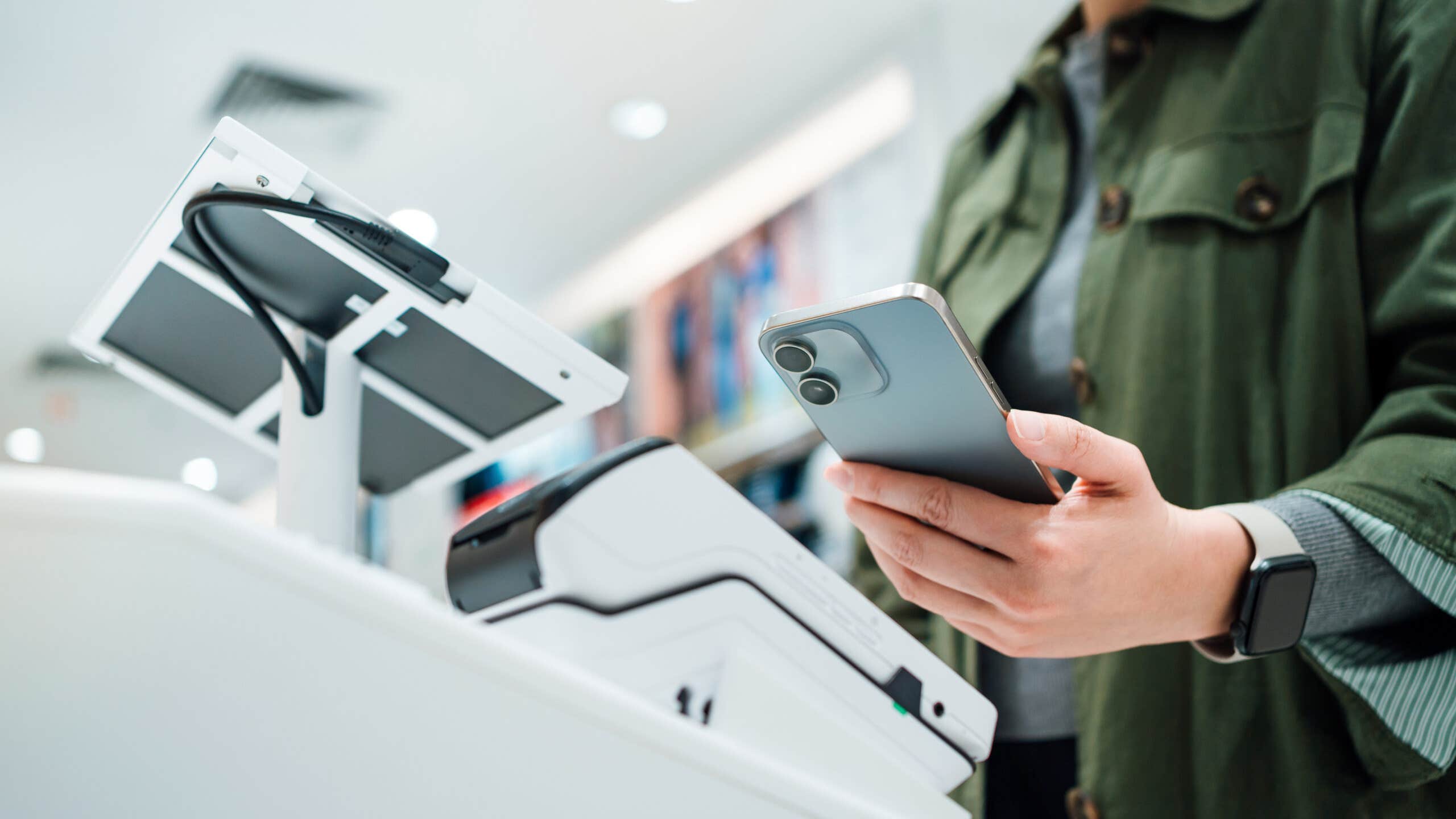 Close up of a person's hand making mobile payment with a smartphone at a self-checkout counter.,