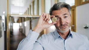 Businessman covering eye with bitcoin while standing at office