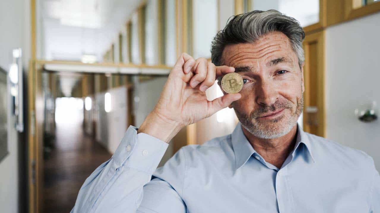 Businessman covering eye with bitcoin while standing at office