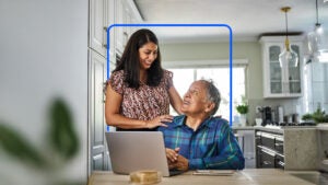 A daughter and mother look at each other while working on a laptop computer.