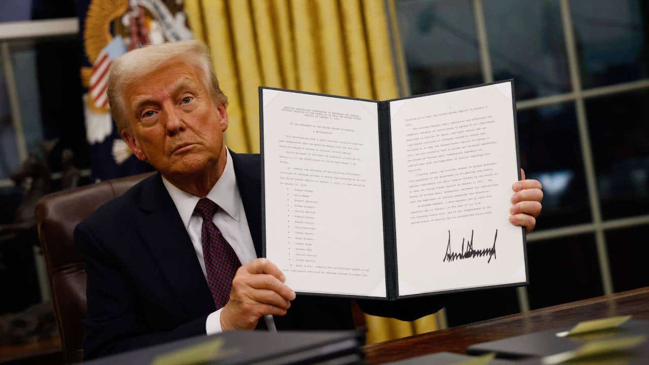 Donald Trump sitting in the Oval Office and holding up an executive order he just signed.