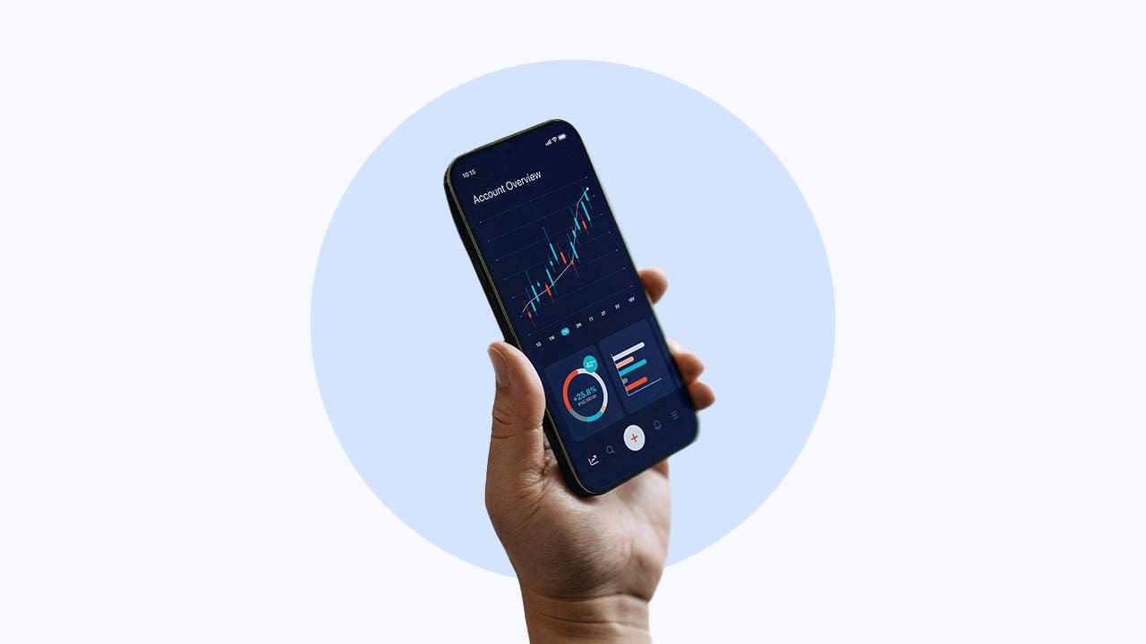 A hand holds up a phone with a stock chart on the screen.