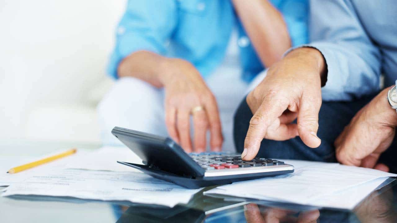 Two people pointing at paperwork with a calculator on top of it.