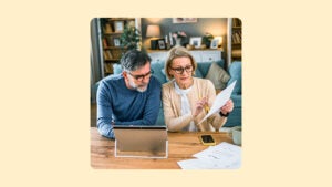 An older couple look at paperwork in front of a laptop computer at home.