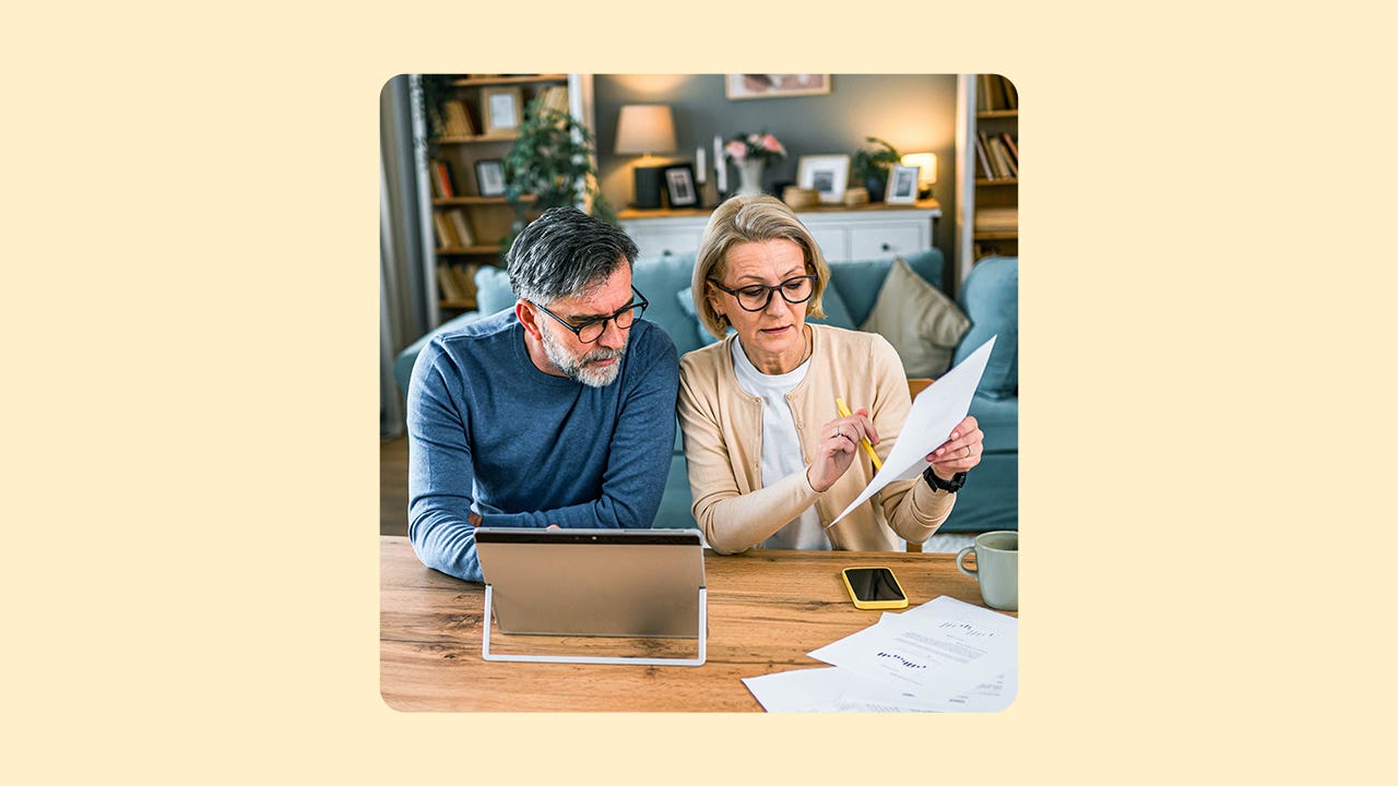 An older couple look at paperwork in front of a laptop computer at home.