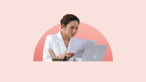 Young woman focused on reading paperwork while looking at laptop screen.