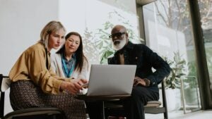 A group of three people sit around a laptop.