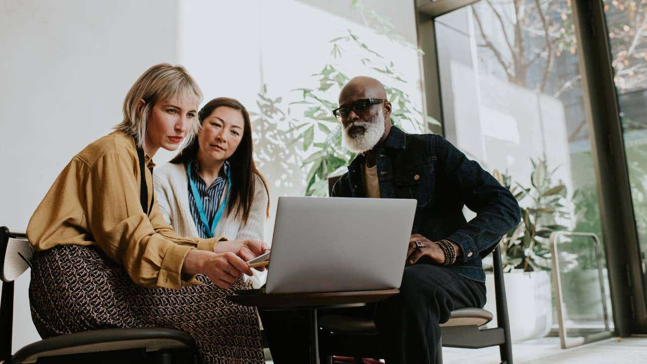 A group of three people sit around a laptop.