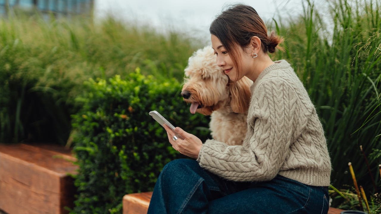 Young Asian woman using smartphone with her dog sitting at city park