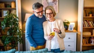 An older couple looks at a cell phone in their living room.