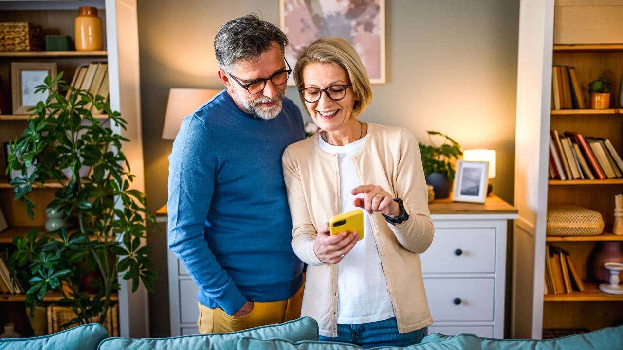 An older couple looks at a cell phone in their living room.