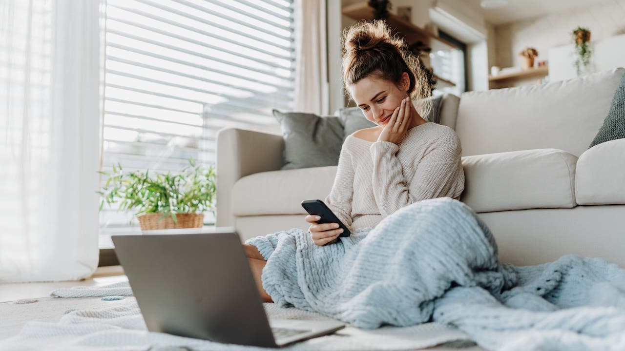 Young woman resting in living room with smartphone and laptop.