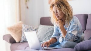 A woman sits on her couch looking at her laptop.