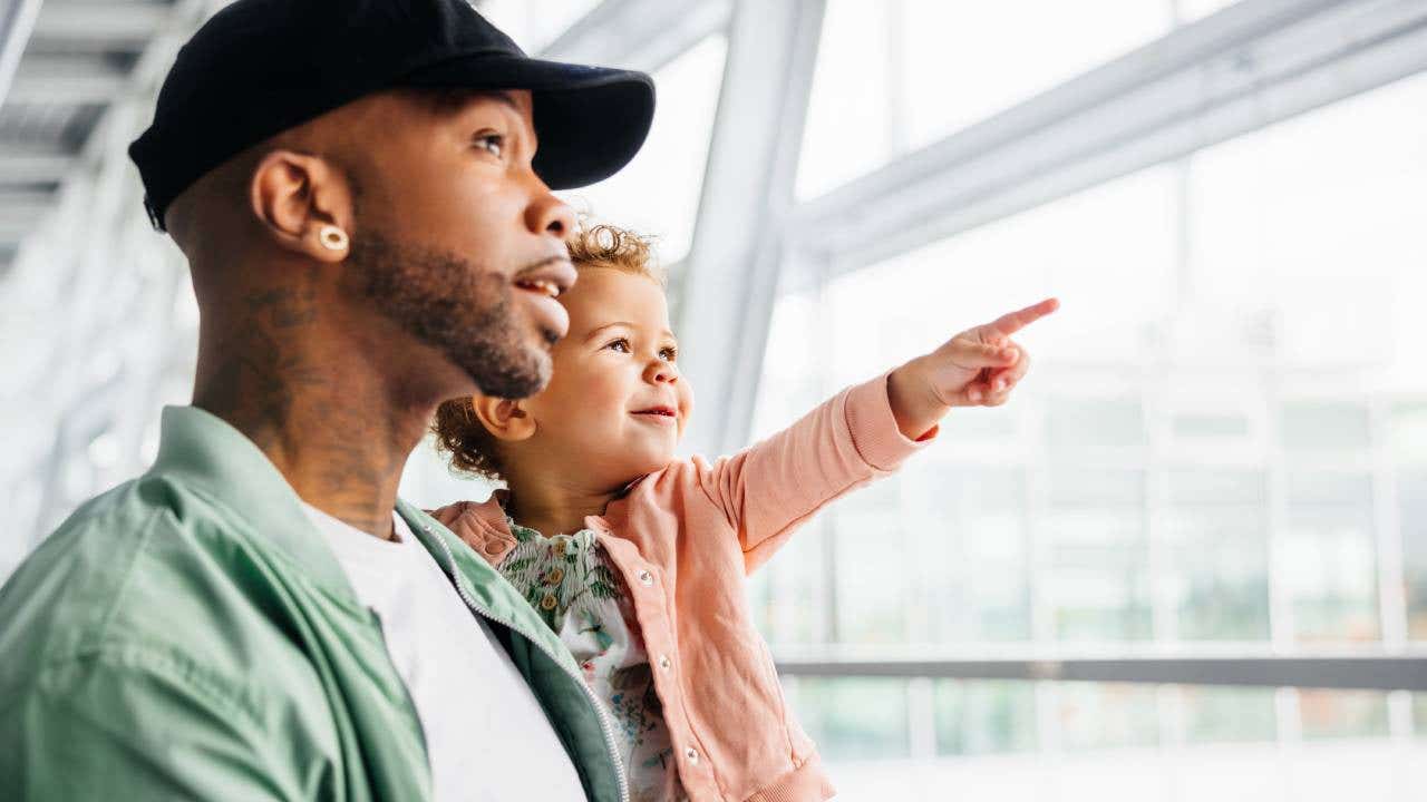 A man holds his child up to a window while the child points outside.