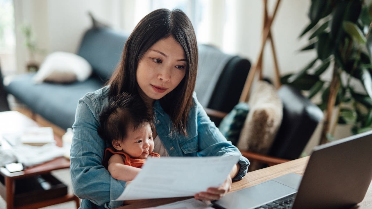 Mother doing paperwork and working at computer while holding baby