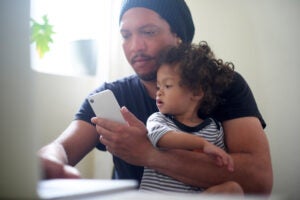 Man works on laptop while holding a child