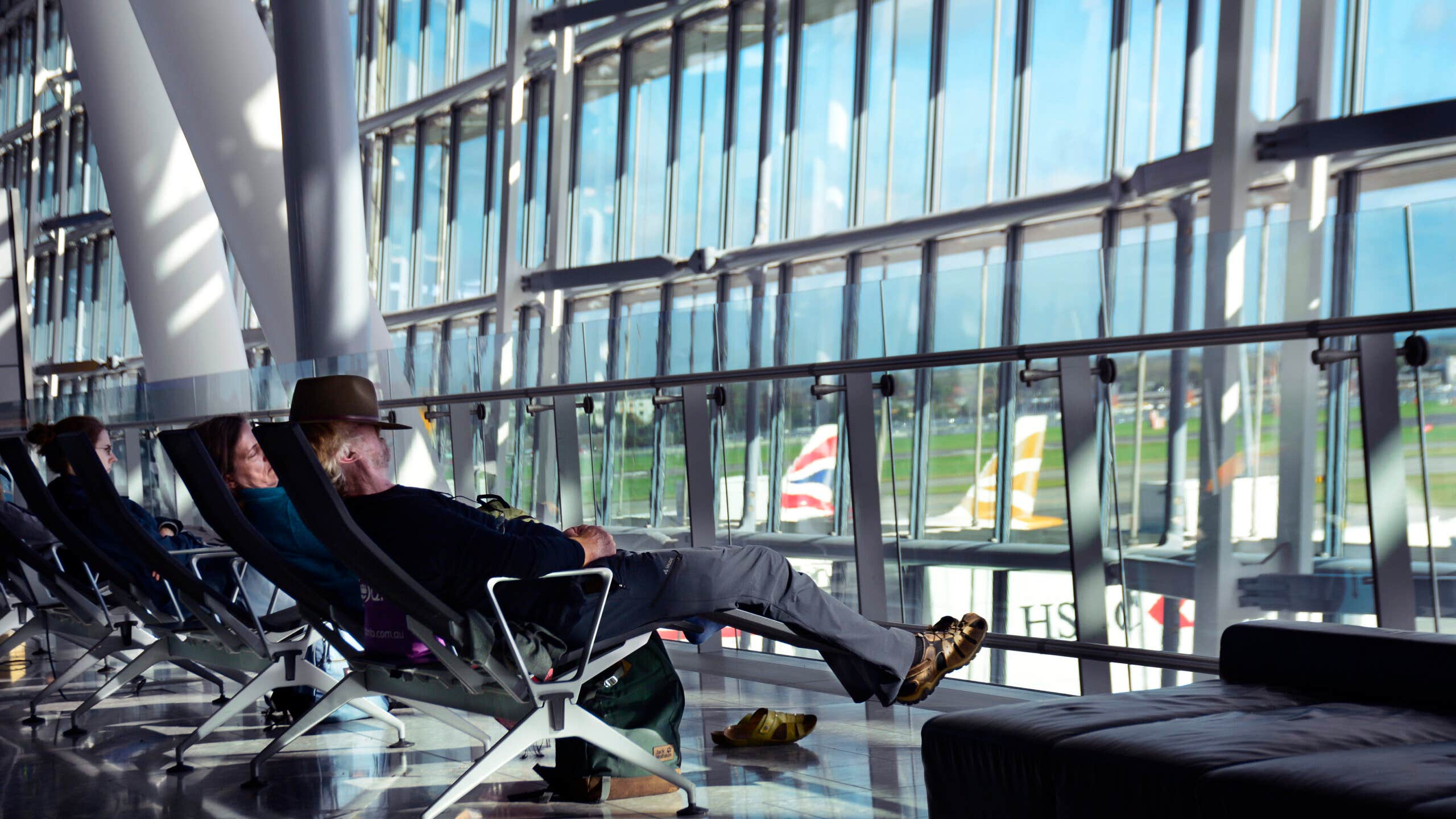 Travelers sit at airport gate looking out windows