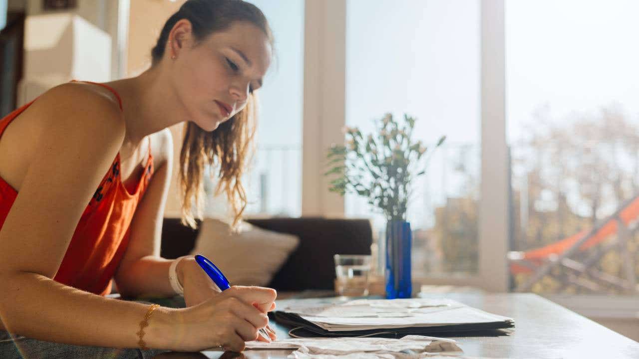 A woman works on her financial accounts at home on a sunny afternoon.