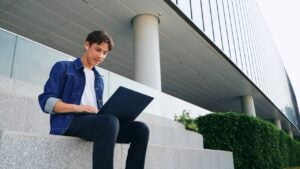 A young man sits outside and works on his laptop.