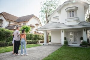 A three-member family is seen in the front of their house, looking at their home, pleased to be homeowners.