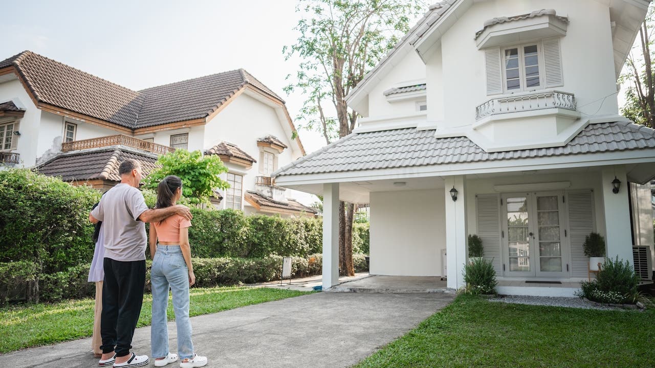 A three-member family is seen in the front of their house, looking at their home, pleased to be homeowners.