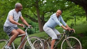 A senior couple rides bikes through a park.