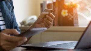 A woman using a laptop holding a credit card and a smartphone in her hands