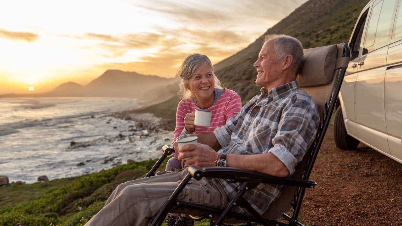 A retirement-age couple enjoys coffee while looking out at the ocean.