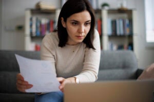 Woman reviewing financial documents while sitting at her laptop at home