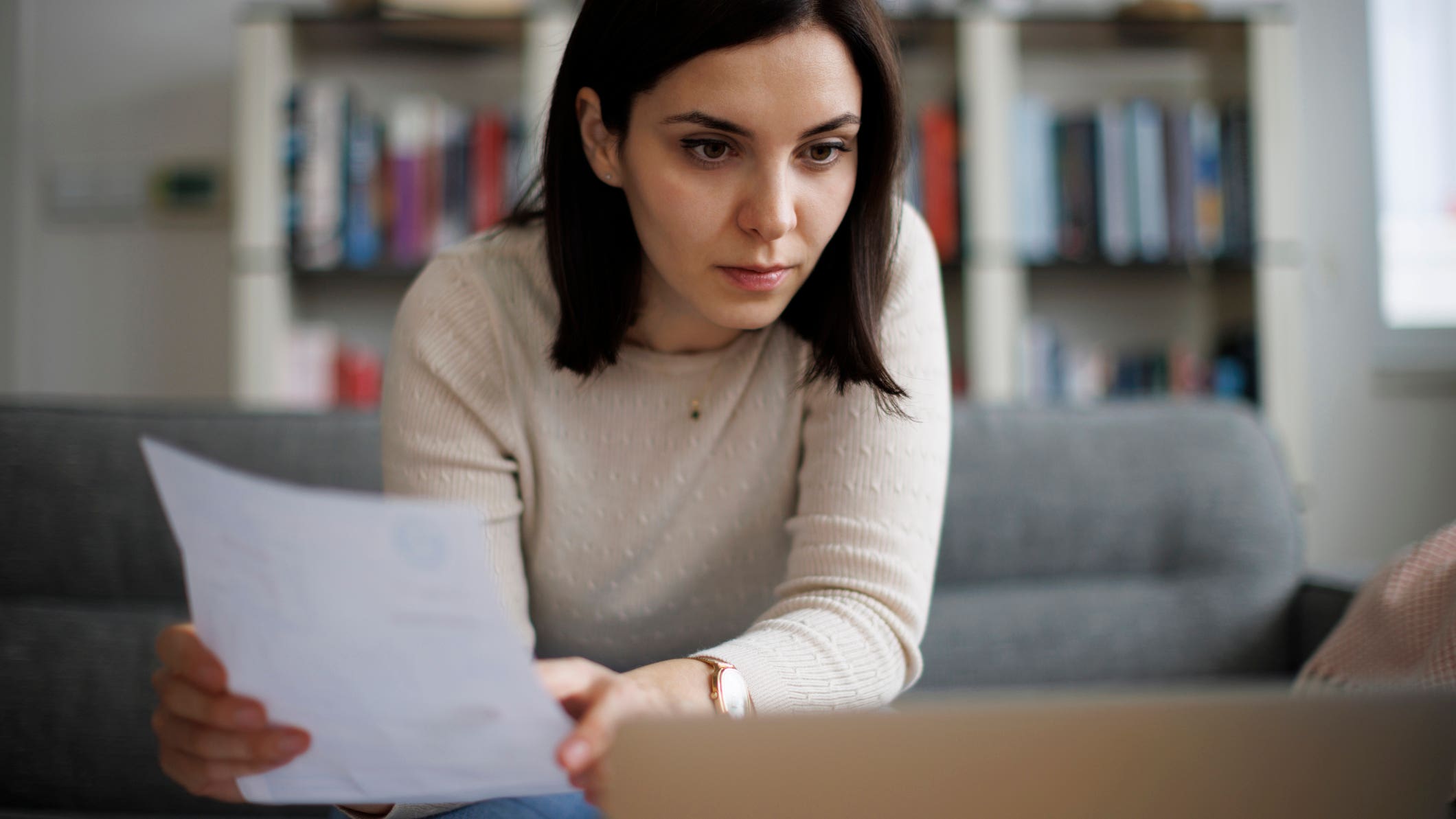 Woman reviewing financial documents while sitting at her laptop at home