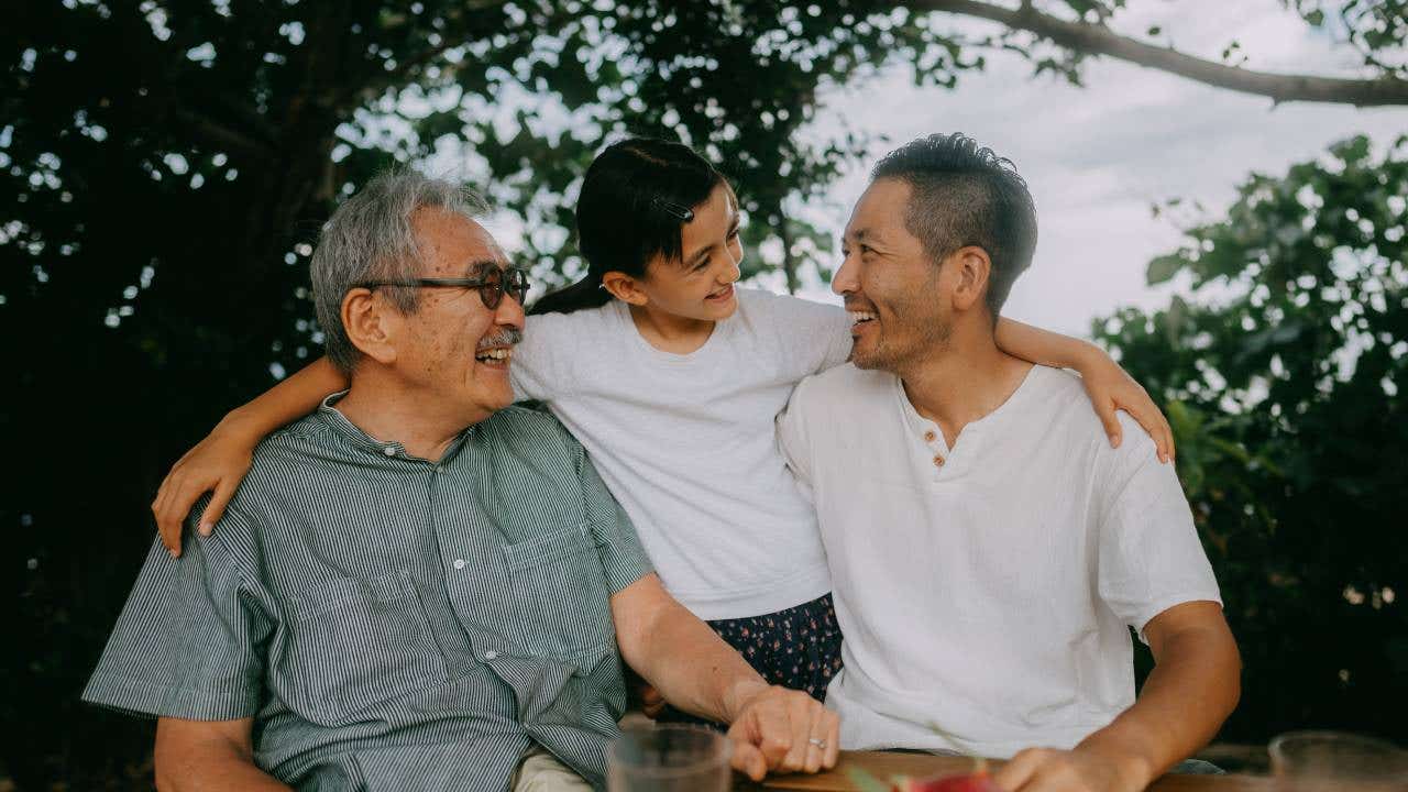 Three generations of a family smile at each other outside.