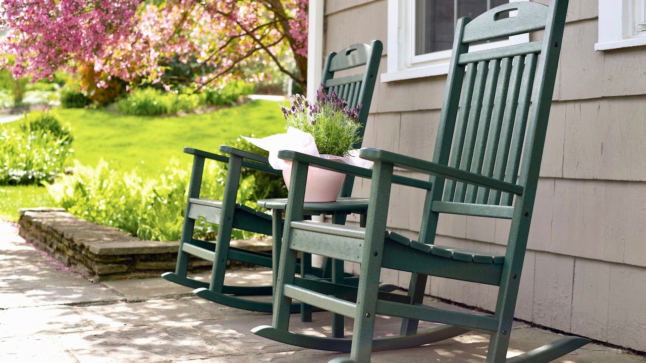 Two green rocking chairs on the porch of a residential home on spring day