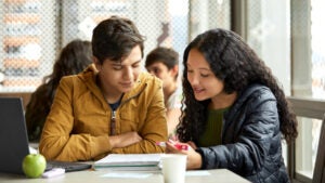 A young man looks thoughtful while reviewing school notes with a young woman.