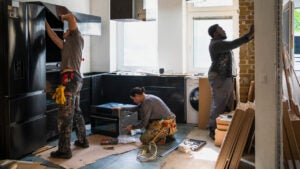 Three adults working on remodeling a kitchen.