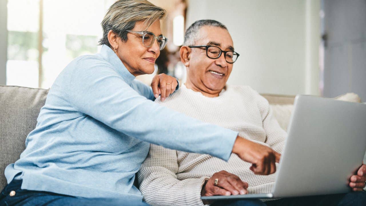 Older couple on a couch, smiling, looking at a laptop