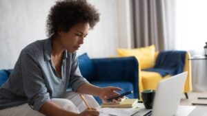 A woman works on her taxes with a laptop and smartphone.