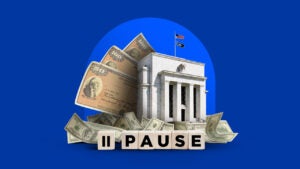 A photo of the Federal Reserve building sits on a blue background with money and blocks that spell pause around it.